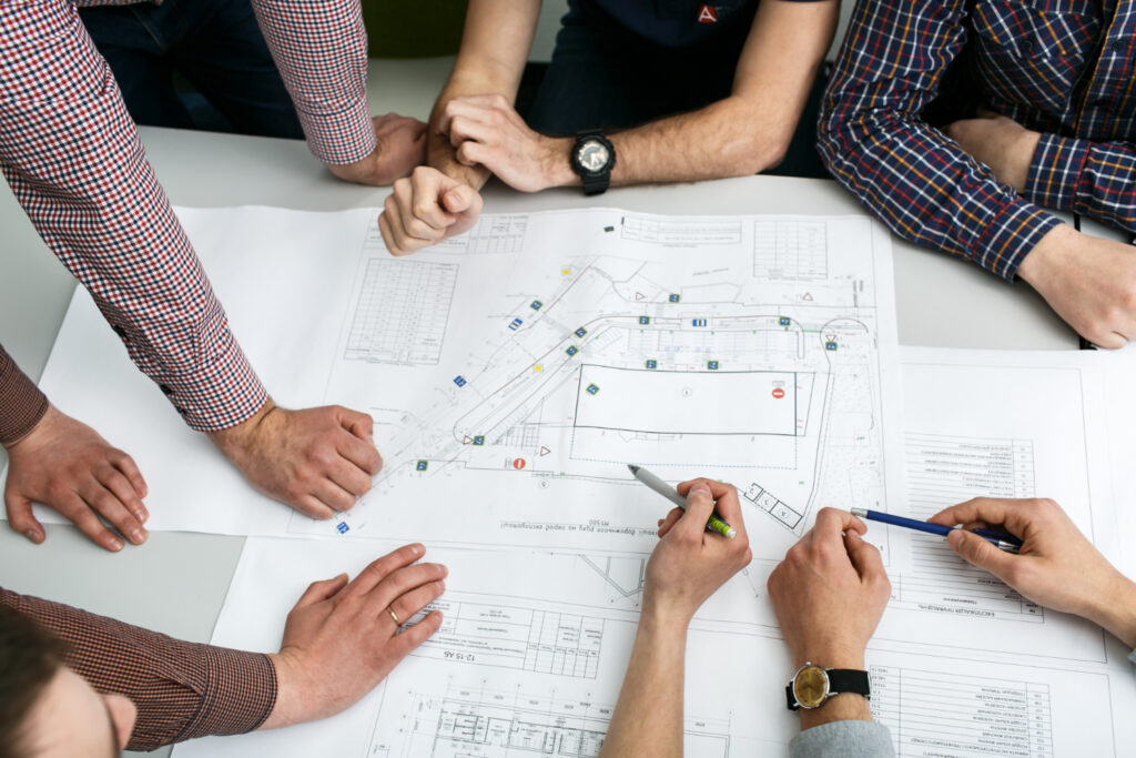 Table with blueprints and hands holding pencils