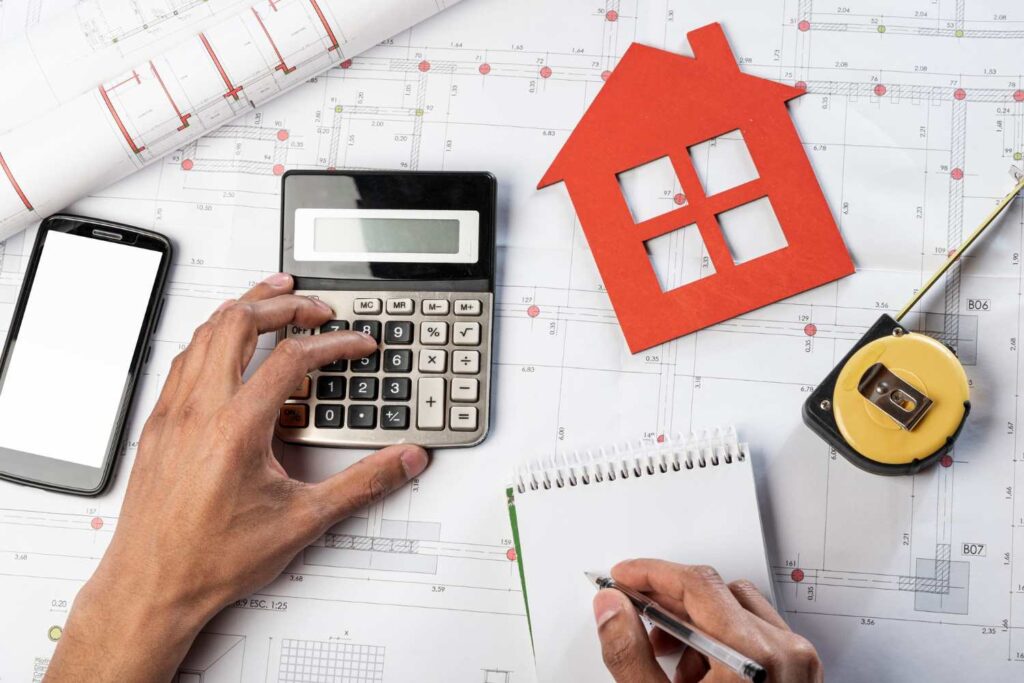 Top view hands and stationery items calculating budget for home construction in calculator